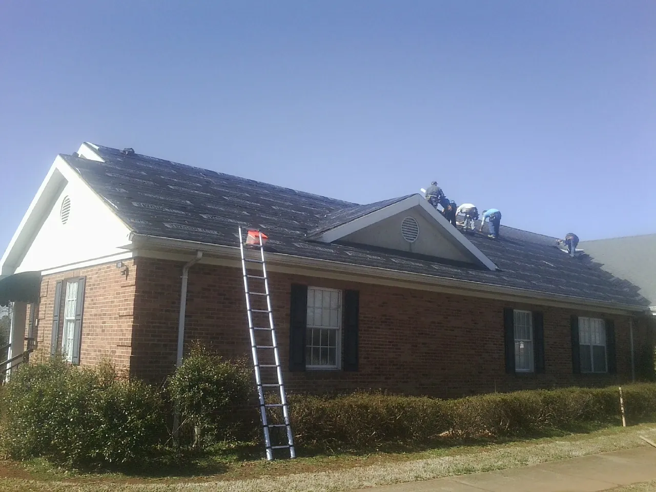 Crew tearing shingles off a brick ranch roof with a ladder set — Metal Roof Repair work by our crew in Hood