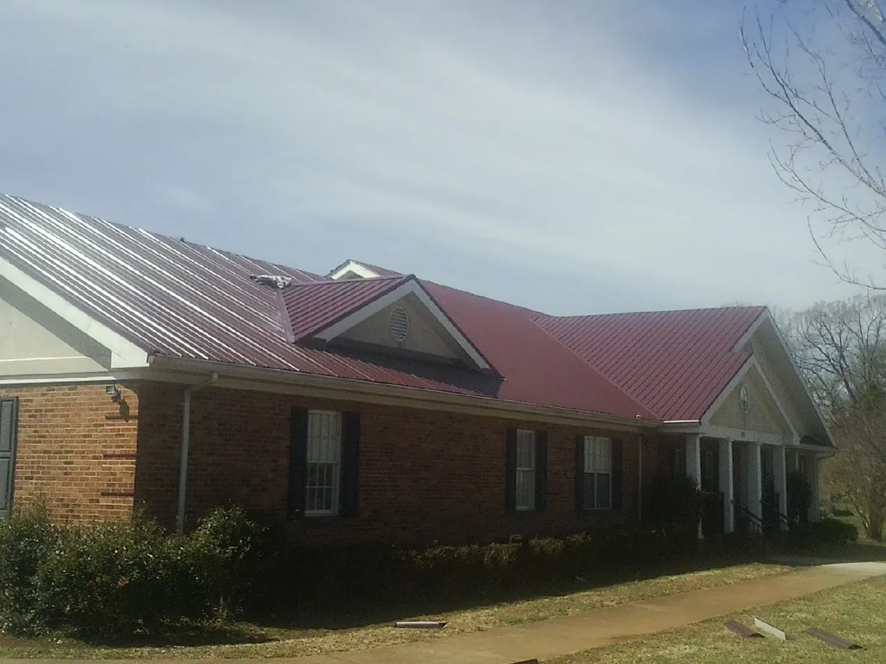 Red metal roof with gabled entries on a long brick building, from a Hail Damage Roof Repair job in Hood