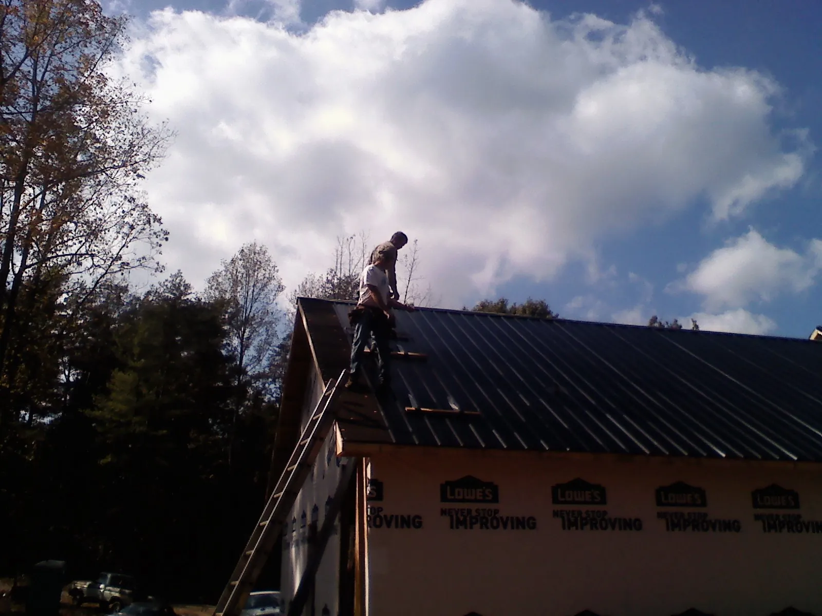 Roofer fastening dark metal panels high against a cloudy sky, from a Roof Inspection job in Hood