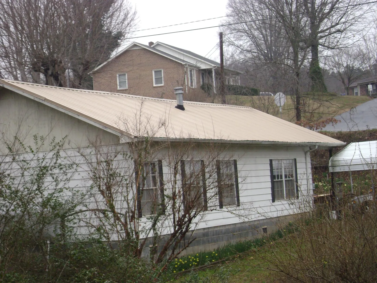 Tan metal roof on a white sided house set into a hillside — Commercial Roofing by Roofing Brothers in Hood